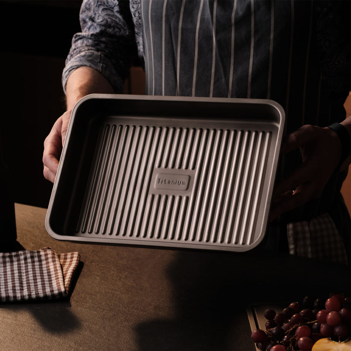 Person holding a rectangular baking tray with a brand logo on a dark background