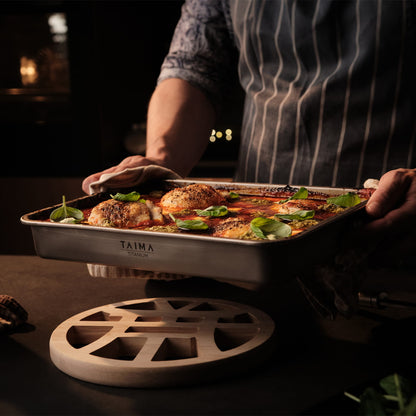 Person holding a titanium tray of food with Taima branding in a dimly lit setting