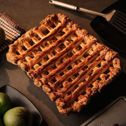 Lattice-topped pie on a dark surface with a spatula and apples in the background