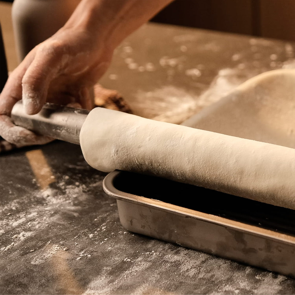 Person rolling out dough with a rolling pin on a floured surface.