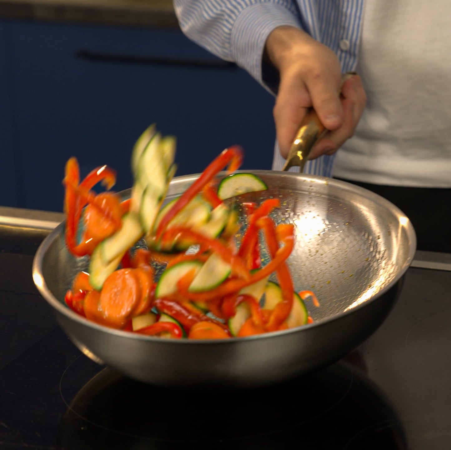 Person cooking sliced vegetables in a pan on a stove